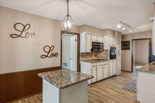 kitchen featuring hanging light fixtures, tasteful backsplash, wood walls, light hardwood / wood-style floors, and black oven