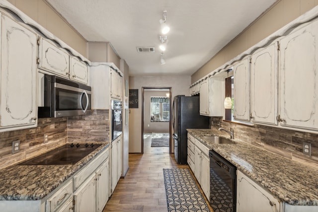 kitchen with dark stone counters, white cabinets, black appliances, and dark hardwood / wood-style floors