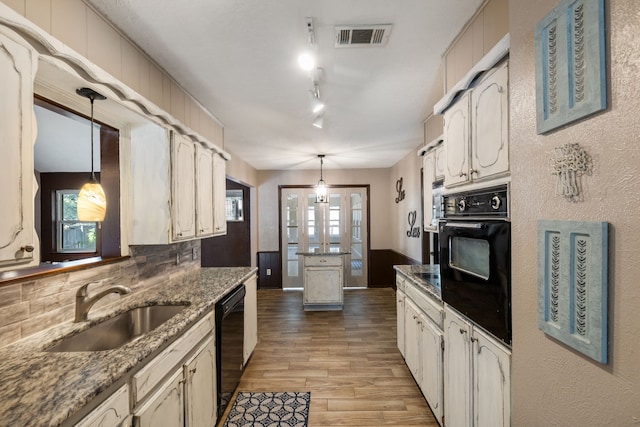 kitchen featuring sink, dark stone countertops, hanging light fixtures, black appliances, and light wood-type flooring