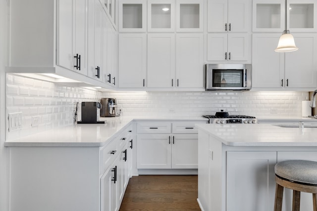 kitchen with pendant lighting, white cabinets, dark hardwood / wood-style floors, appliances with stainless steel finishes, and a breakfast bar area