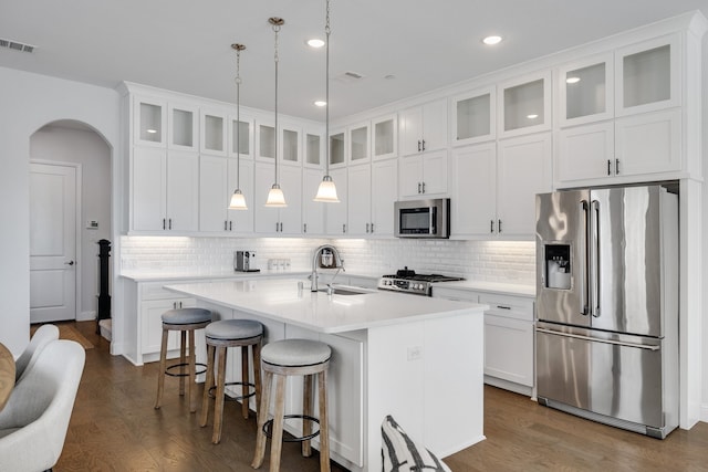 kitchen with an island with sink, appliances with stainless steel finishes, decorative light fixtures, dark hardwood / wood-style flooring, and white cabinetry