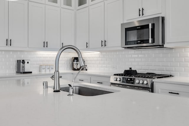 kitchen with decorative backsplash, white cabinetry, sink, and appliances with stainless steel finishes