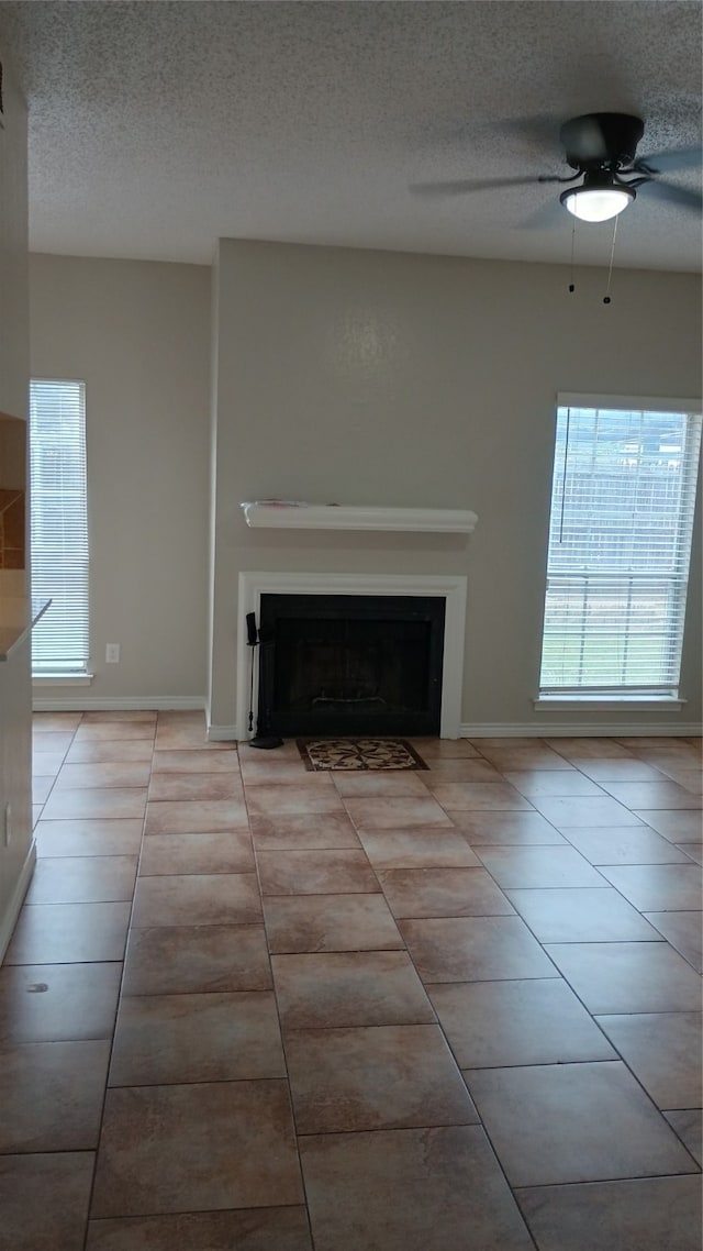 unfurnished living room with ceiling fan, light tile patterned flooring, and a textured ceiling