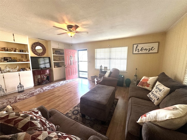 living room featuring built in shelves, ceiling fan, wood-type flooring, and a textured ceiling