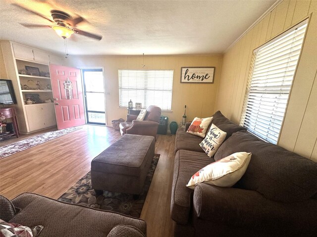 living room featuring ceiling fan, built in features, wood-type flooring, and a textured ceiling