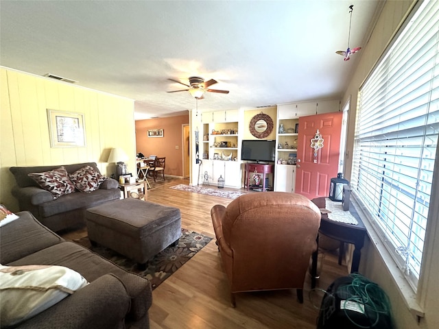 living room featuring wood-type flooring, ceiling fan, and built in shelves