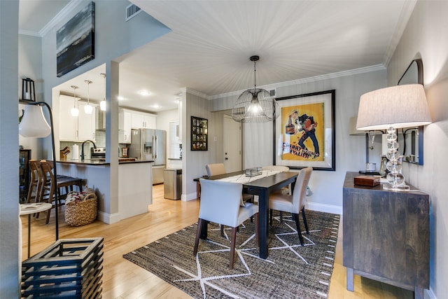 dining space featuring light hardwood / wood-style floors, crown molding, and sink