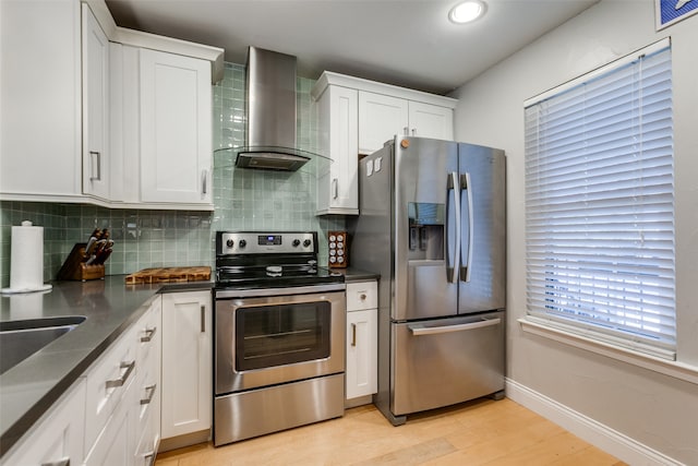 kitchen with white cabinets, appliances with stainless steel finishes, tasteful backsplash, wall chimney range hood, and light wood-type flooring