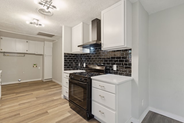 kitchen with white cabinets, black gas range, light hardwood / wood-style flooring, and wall chimney range hood