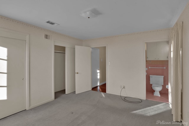 unfurnished bedroom featuring light colored carpet, ensuite bath, and a closet