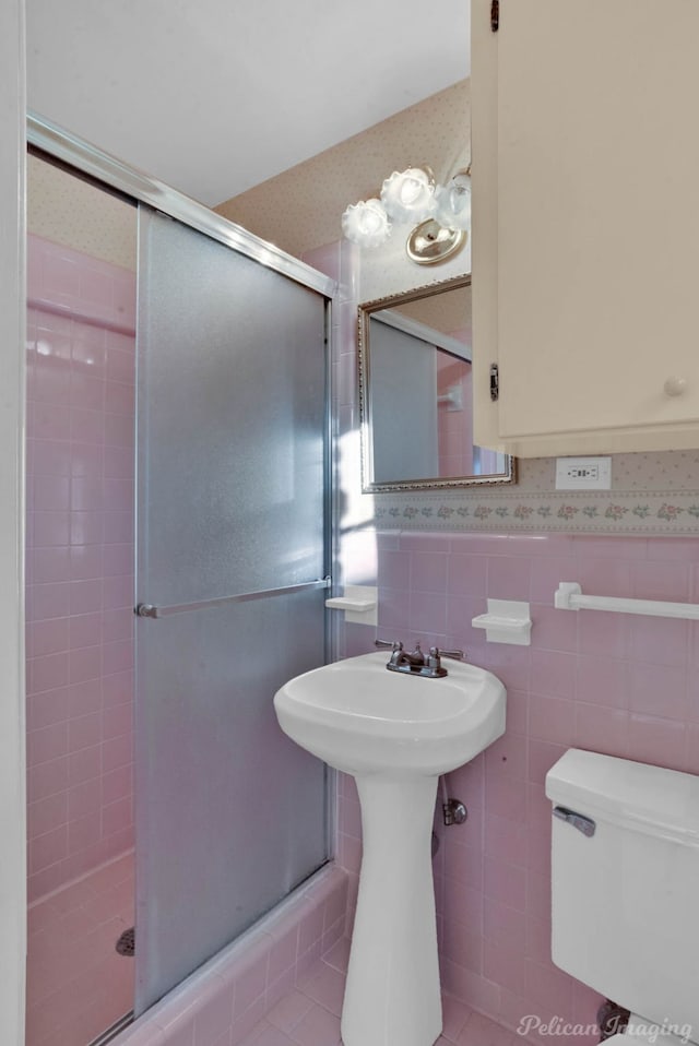 bathroom with a shower with door, tile patterned flooring, tile walls, and toilet