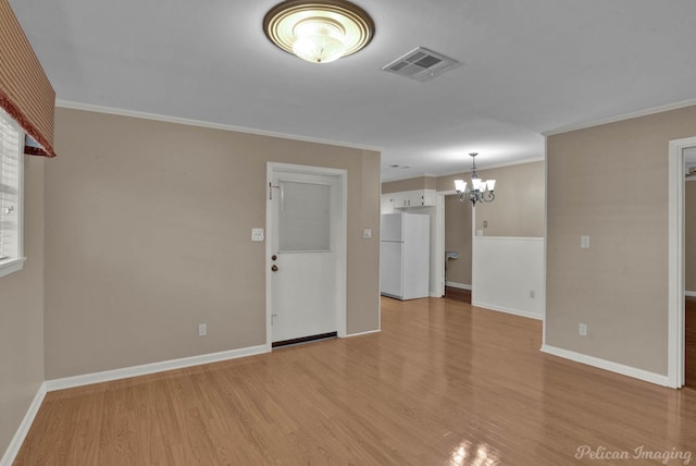 spare room featuring ornamental molding, light wood-type flooring, and an inviting chandelier