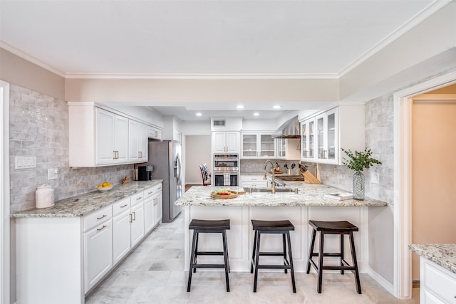 kitchen featuring decorative backsplash, light stone countertops, stainless steel appliances, white cabinets, and a breakfast bar area