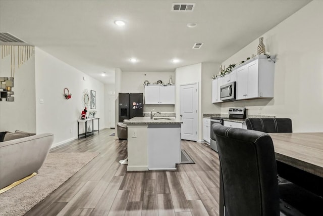 kitchen featuring white cabinetry, a kitchen island with sink, hardwood / wood-style flooring, and appliances with stainless steel finishes