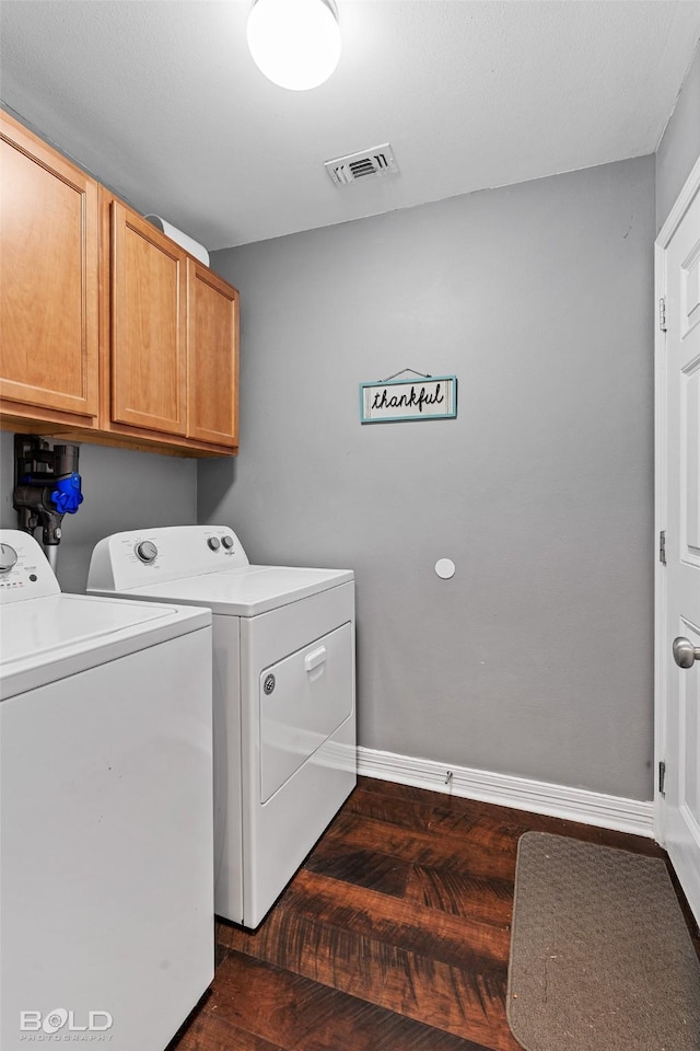 laundry area featuring washing machine and clothes dryer, dark wood-type flooring, and cabinets