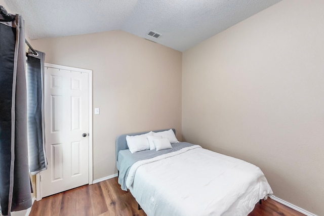 bedroom with a textured ceiling, lofted ceiling, and dark wood-type flooring