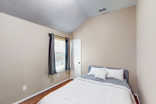 bedroom with a textured ceiling, dark hardwood / wood-style flooring, and lofted ceiling