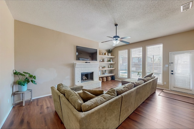 living room featuring a fireplace, a textured ceiling, ceiling fan, and dark wood-type flooring