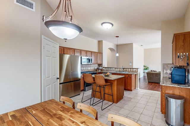 kitchen featuring sink, tasteful backsplash, light hardwood / wood-style floors, decorative light fixtures, and appliances with stainless steel finishes