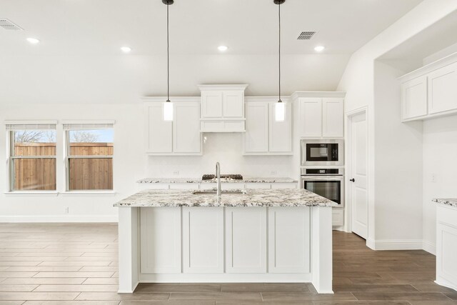 kitchen featuring a center island with sink, lofted ceiling, dark hardwood / wood-style flooring, stainless steel appliances, and light stone counters