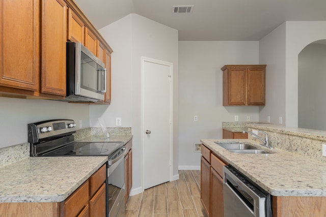 kitchen with light stone counters, sink, light wood-type flooring, and appliances with stainless steel finishes