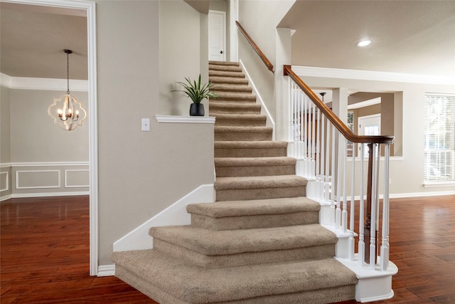 staircase with crown molding, hardwood / wood-style floors, and a chandelier