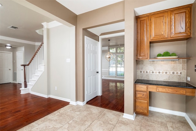 kitchen with dark stone countertops, crown molding, light wood-type flooring, and tasteful backsplash