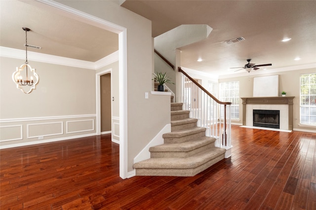 staircase featuring ceiling fan with notable chandelier, hardwood / wood-style flooring, crown molding, and a tiled fireplace