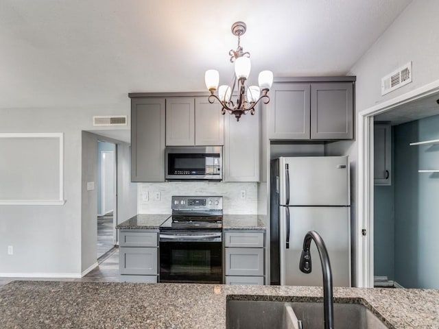 kitchen featuring appliances with stainless steel finishes, tasteful backsplash, dark stone countertops, a chandelier, and gray cabinets