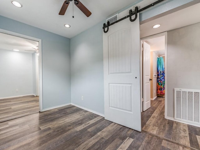 bedroom with a barn door, dark hardwood / wood-style floors, a closet, and ceiling fan