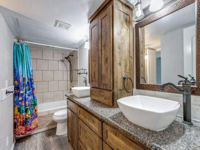 full bathroom with hardwood / wood-style floors, a textured ceiling, toilet, vanity, and shower / tub combo