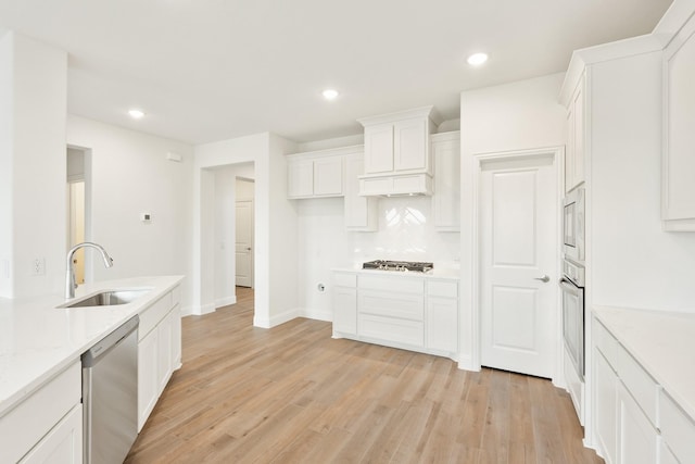 kitchen featuring appliances with stainless steel finishes, light wood-type flooring, light stone countertops, sink, and white cabinetry