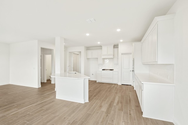 kitchen with sink, light hardwood / wood-style floors, white cabinets, gas cooktop, and a kitchen island with sink