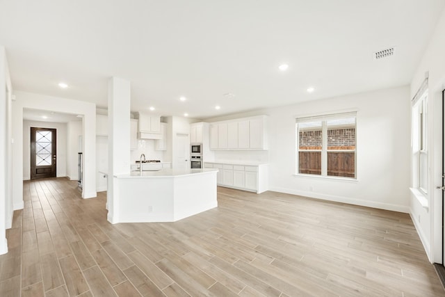 kitchen featuring built in microwave, light wood-type flooring, sink, white cabinetry, and a kitchen island with sink