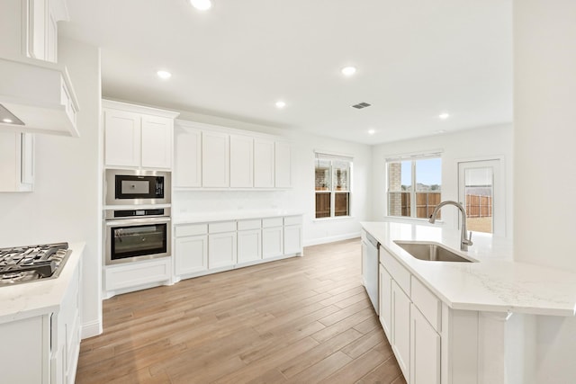 kitchen featuring light wood-type flooring, white cabinetry, stainless steel appliances, sink, and light stone counters