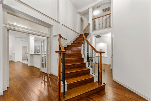 staircase with ornate columns, a towering ceiling, and wood-type flooring