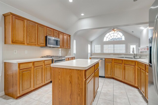 kitchen featuring sink, vaulted ceiling, light tile patterned floors, appliances with stainless steel finishes, and a center island