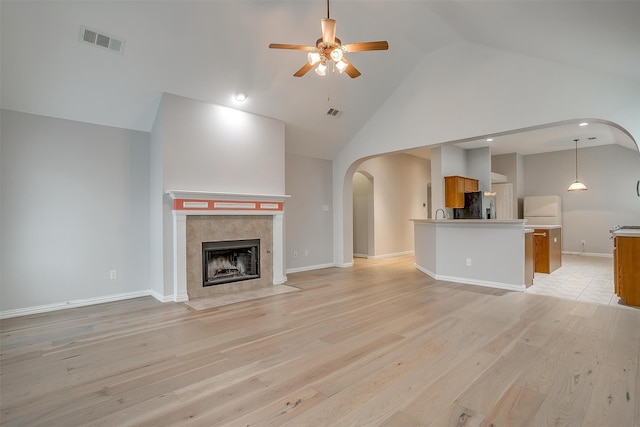 unfurnished living room featuring a fireplace, light wood-type flooring, high vaulted ceiling, and ceiling fan