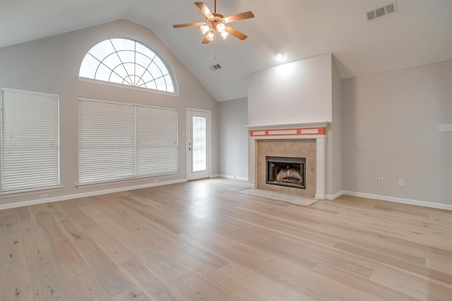 unfurnished living room with a tiled fireplace, ceiling fan, plenty of natural light, and light wood-type flooring