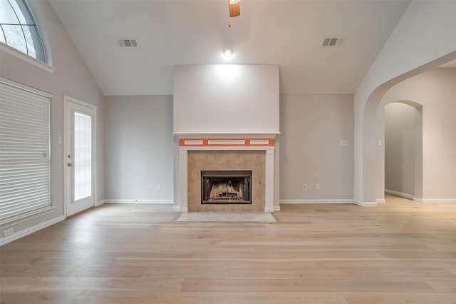 unfurnished living room with a tiled fireplace, ceiling fan, light hardwood / wood-style flooring, and high vaulted ceiling