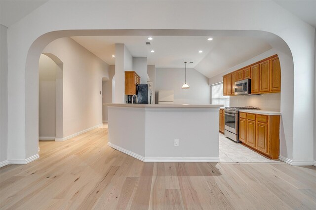 kitchen featuring pendant lighting, vaulted ceiling, a center island, light hardwood / wood-style floors, and stainless steel appliances