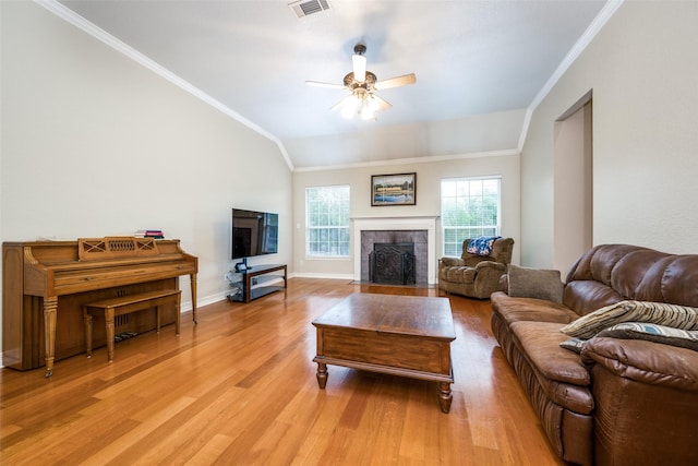 living room featuring a tile fireplace, vaulted ceiling, light hardwood / wood-style flooring, ceiling fan, and ornamental molding