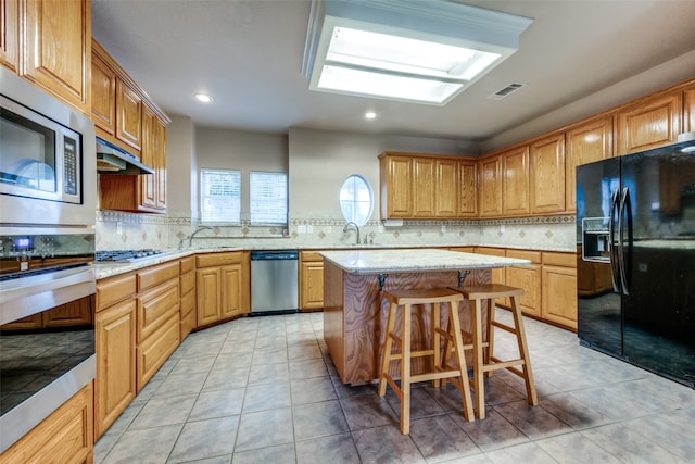 kitchen featuring appliances with stainless steel finishes, backsplash, light tile patterned floors, a kitchen island, and a breakfast bar area