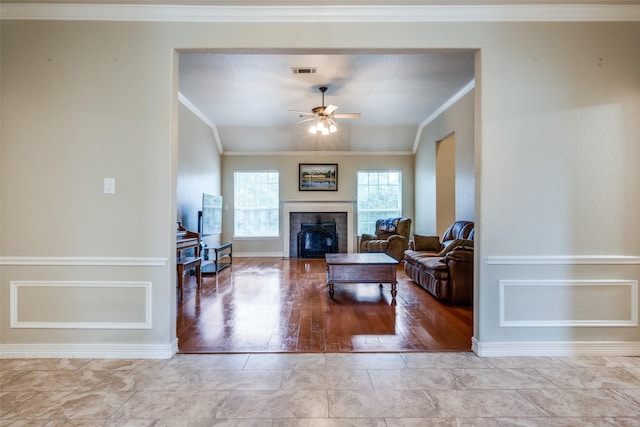 living room with vaulted ceiling, ceiling fan, light wood-type flooring, ornamental molding, and a tiled fireplace