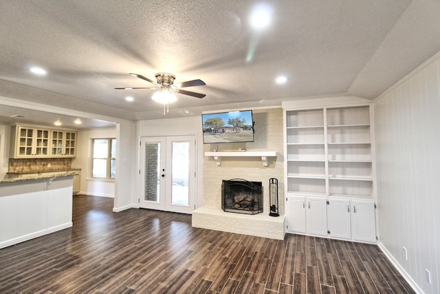 unfurnished living room with ceiling fan, dark wood-style flooring, a textured ceiling, french doors, and a fireplace