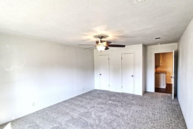 unfurnished bedroom with ceiling fan, two closets, carpet, and a textured ceiling