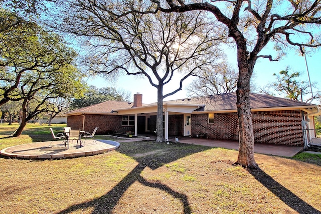 rear view of property with a yard, brick siding, a patio, and a chimney