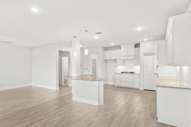 kitchen featuring white cabinetry, light stone countertops, sink, and a center island with sink