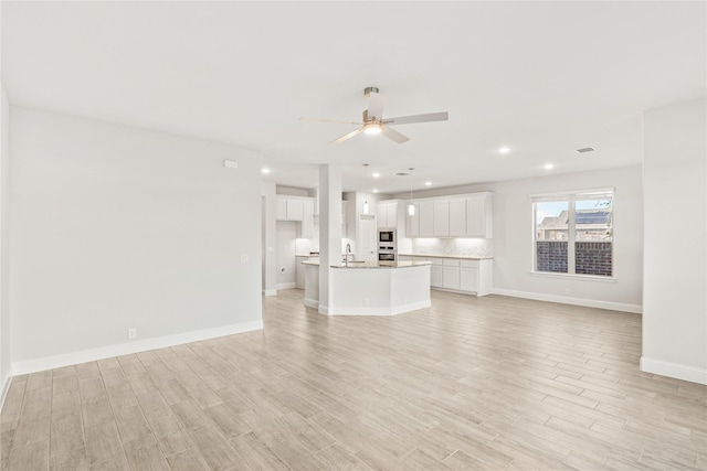 unfurnished living room featuring ceiling fan, sink, and light wood-type flooring