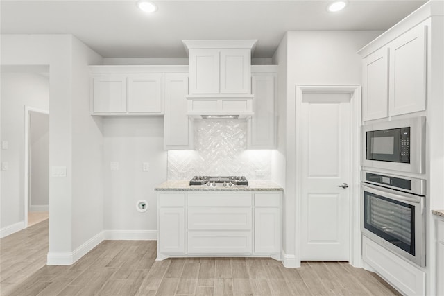 kitchen with white cabinetry, decorative backsplash, appliances with stainless steel finishes, and light stone counters